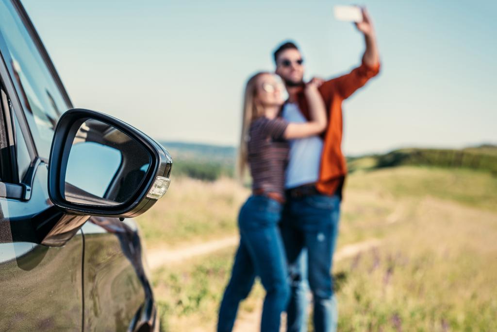vista de cerca del espejo lateral del coche y la pareja tomando selfie sobre fondo borroso
  - Foto, Imagen