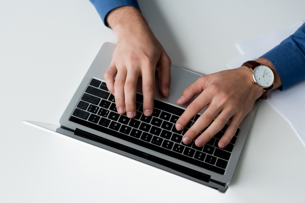 обрізаний знімок людини, що працює з ноутбуком на білій поверхні
 - Фото, зображення