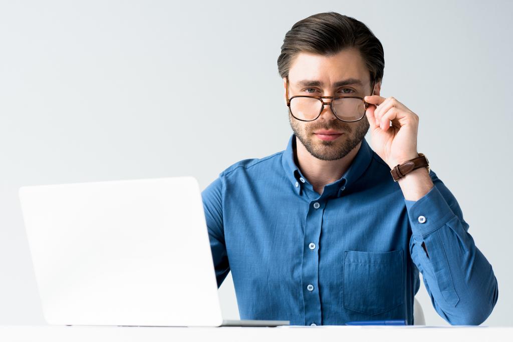 knappe jonge zakenman met laptop zit op de werkplek en kijken naar camera geïsoleerd op wit - Foto, afbeelding