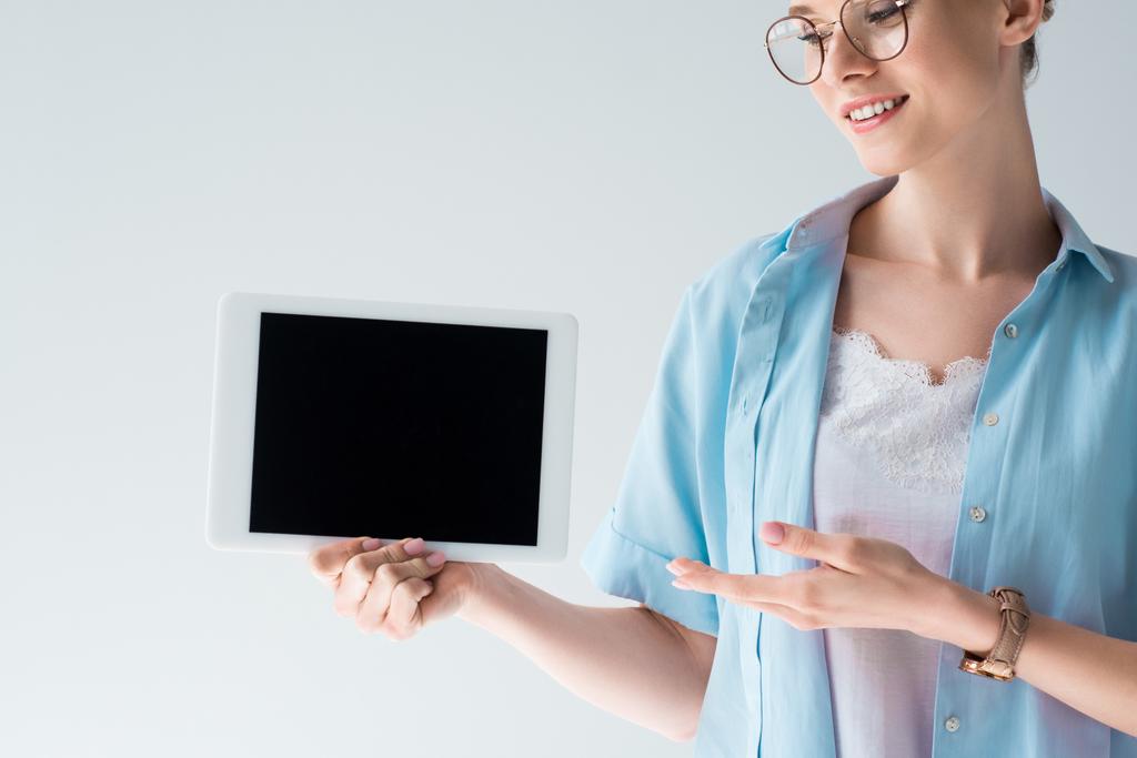 χαμογελαστός, νεαρή γυναίκα δείχνει tablet με κενή οθόνη που απομονώνονται σε γκρι - Φωτογραφία, εικόνα