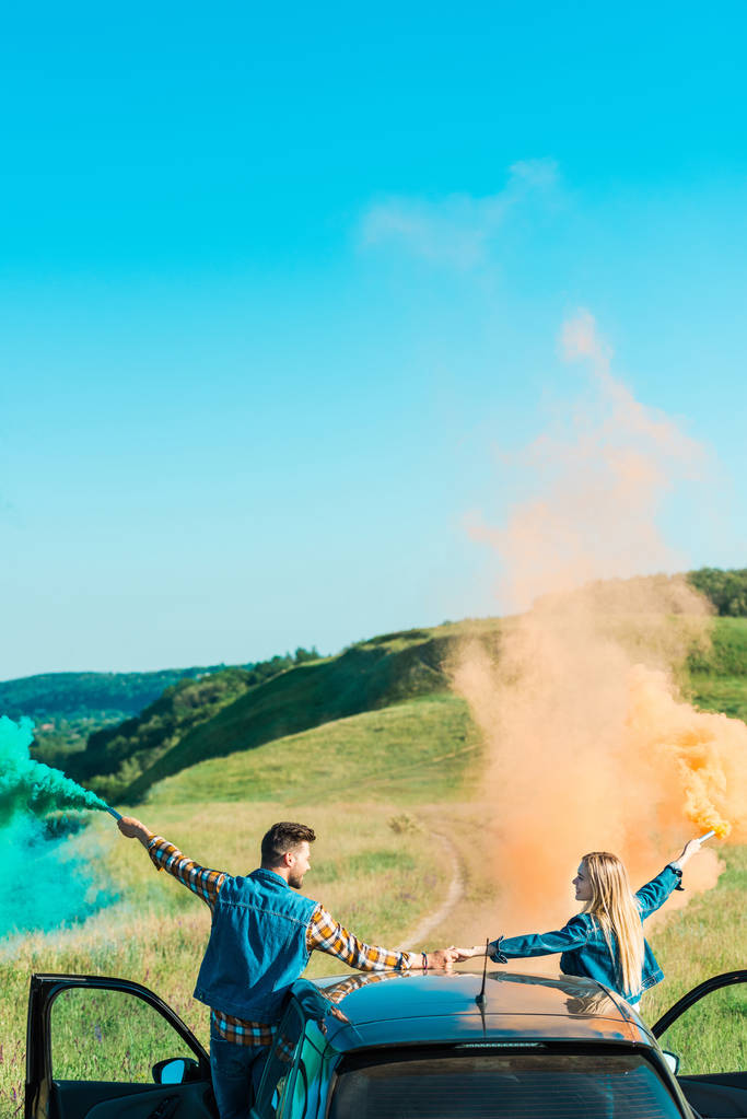  vista trasera de la pareja con bombas de colores de pie en el coche y de la mano en el campo
  - Foto, imagen