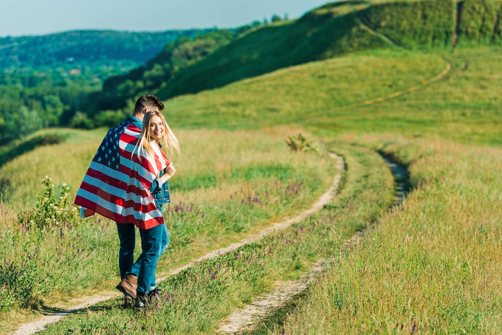 田舎の牧草地、独立記念日のコンセプトにアメリカの国旗と若いカップルの背面します。 - 写真・画像