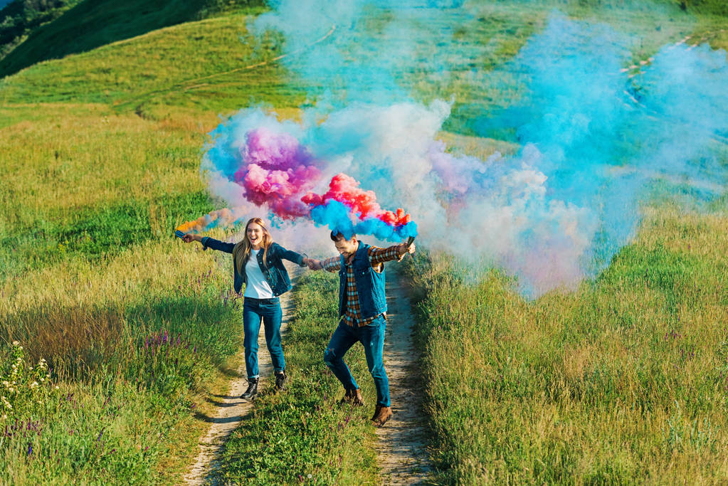 vue grand angle du couple tenant des bombes fumigènes colorées sur prairie rurale
  - Photo, image