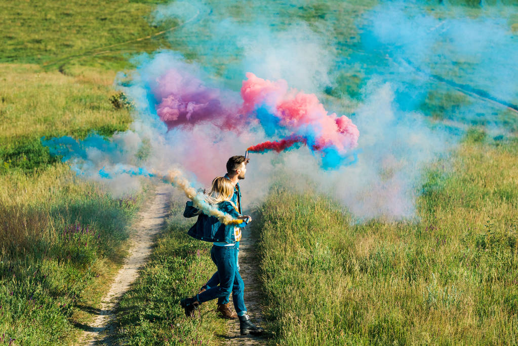 vue latérale du couple tenant des bombes fumigènes colorées dans le champ
 - Photo, image
