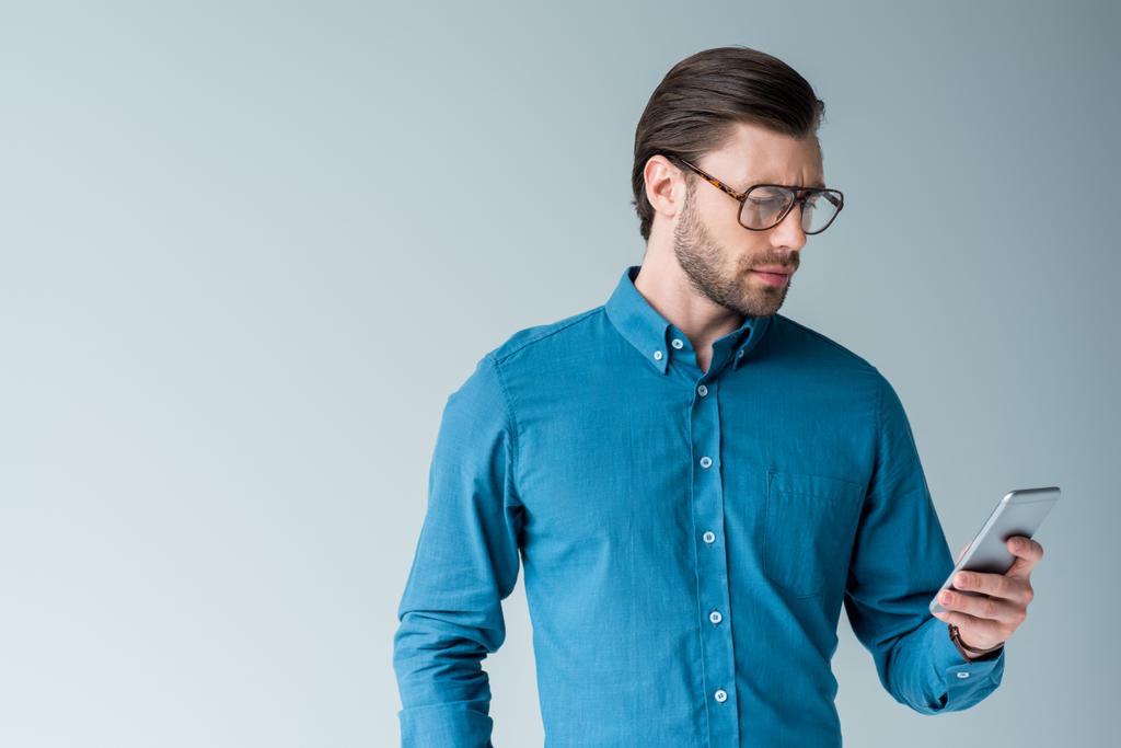 a stílusos szemüvegek használ smartphone elszigetelt fehér komoly fiatalember - Fotó, kép