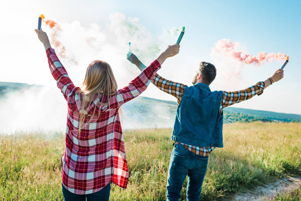 vista trasera de joven pareja sosteniendo coloridas bombas de humo en prado rural
  - Foto, imagen