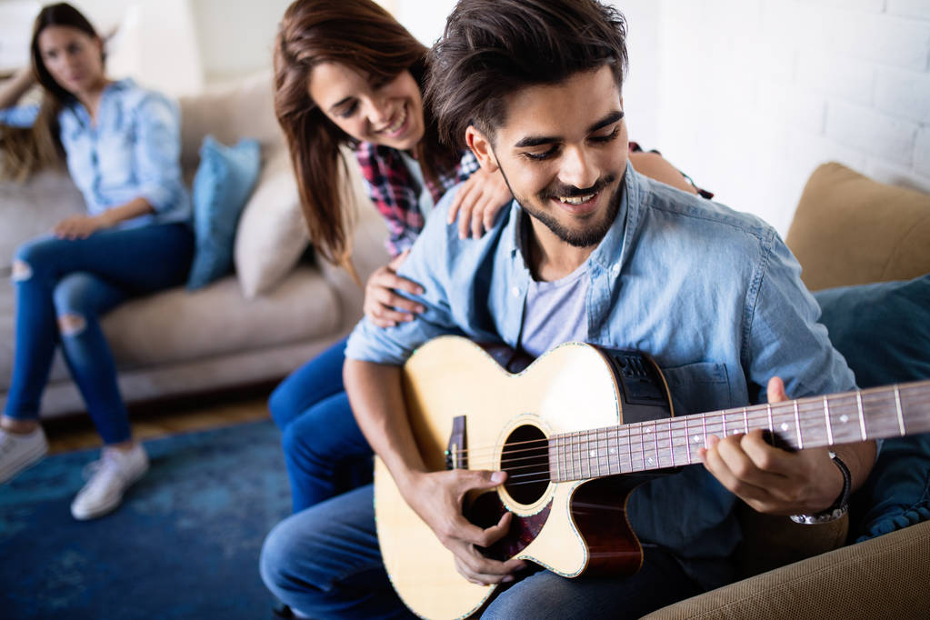 Молодой красивый мужчина играет на гитаре для своей красивой девушки - Фото, изображение