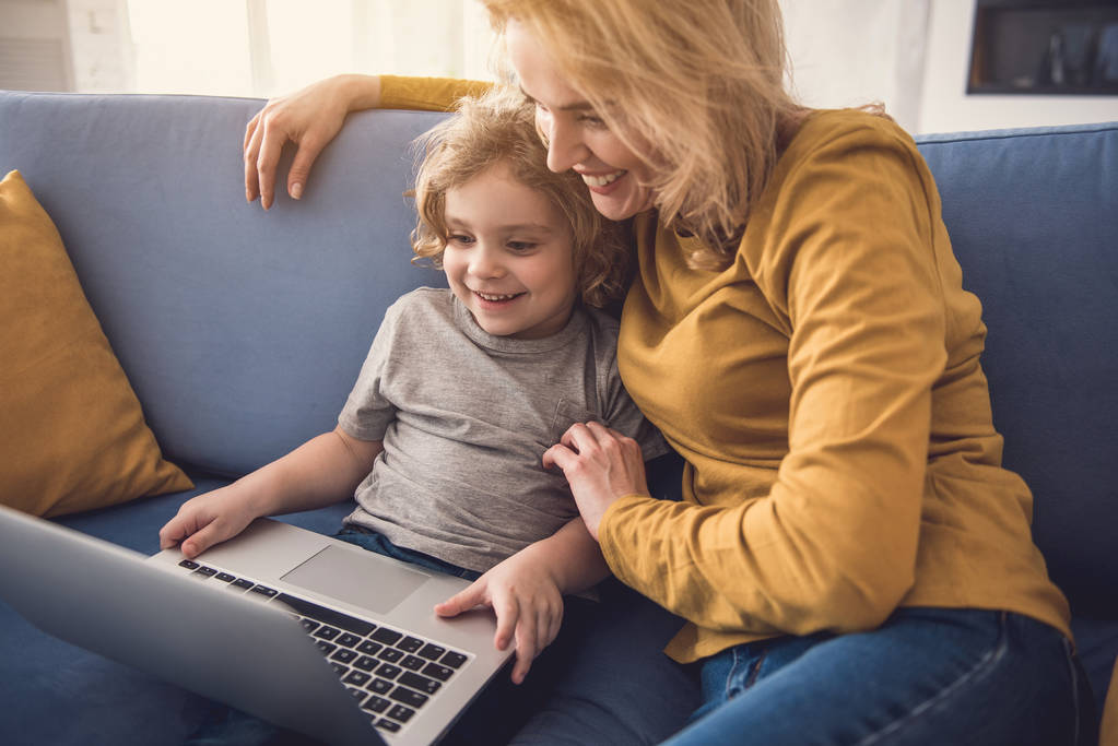 Mosolygó anya és fia élvezik a laptop használ bent - Fotó, kép