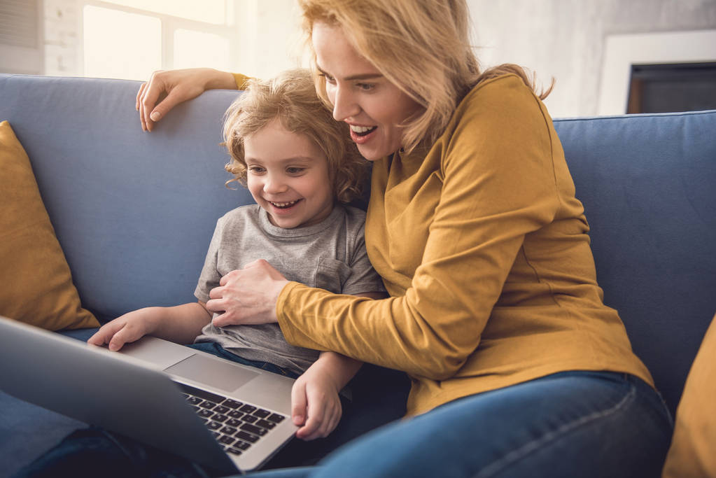 Feliz mamá y su hijo están utilizando el ordenador portátil en la sala de estar
 - Foto, Imagen
