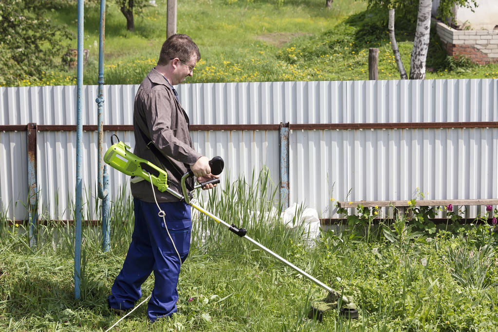 bir trimer gözlüklü bir adam köyde bir ev avlusunda çim mows, ülke topraklarının sipariş getiriyor - Fotoğraf, Görsel