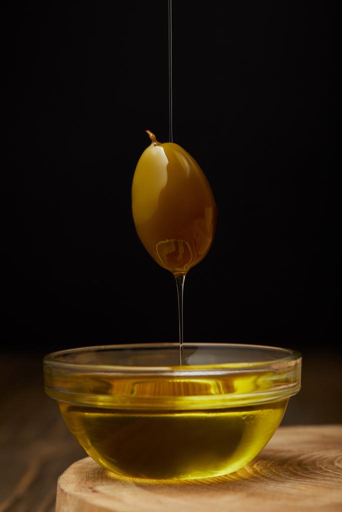 aceite de oliva fresco que gotea de la fruta de oliva por encima del tazón en la superficie de madera
 - Foto, Imagen