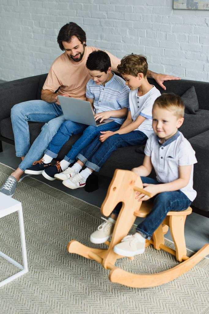 ο άνθρωπος και τα παιδιά κοντά χρησιμοποιώντας το φορητό υπολογιστή μαζί στον καναπέ στο σπίτι - Φωτογραφία, εικόνα