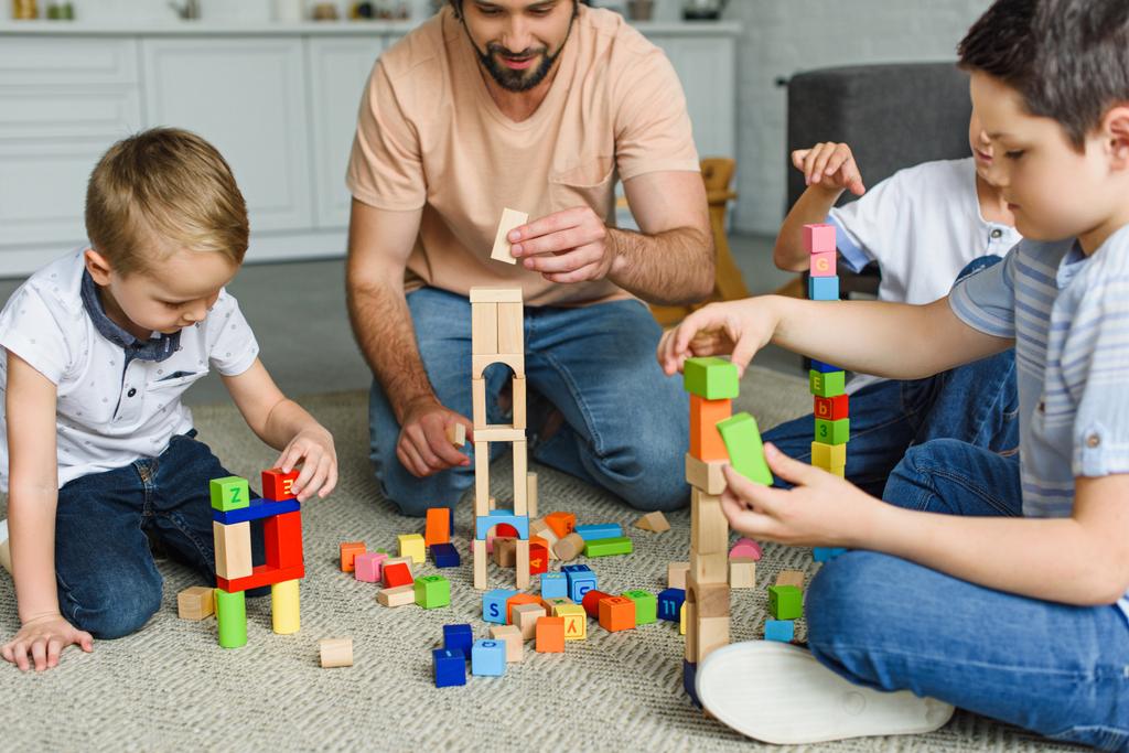 az apa és a gyerekek játszó fadarabot együtt a földre otthon részleges megtekintése - Fotó, kép