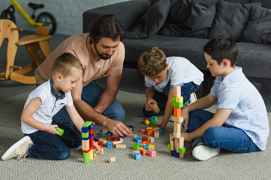 ο πατέρας και τα παιδιά παίζουν με ξύλινα μπλοκ μαζί στο πάτωμα στο σπίτι - Φωτογραφία, εικόνα