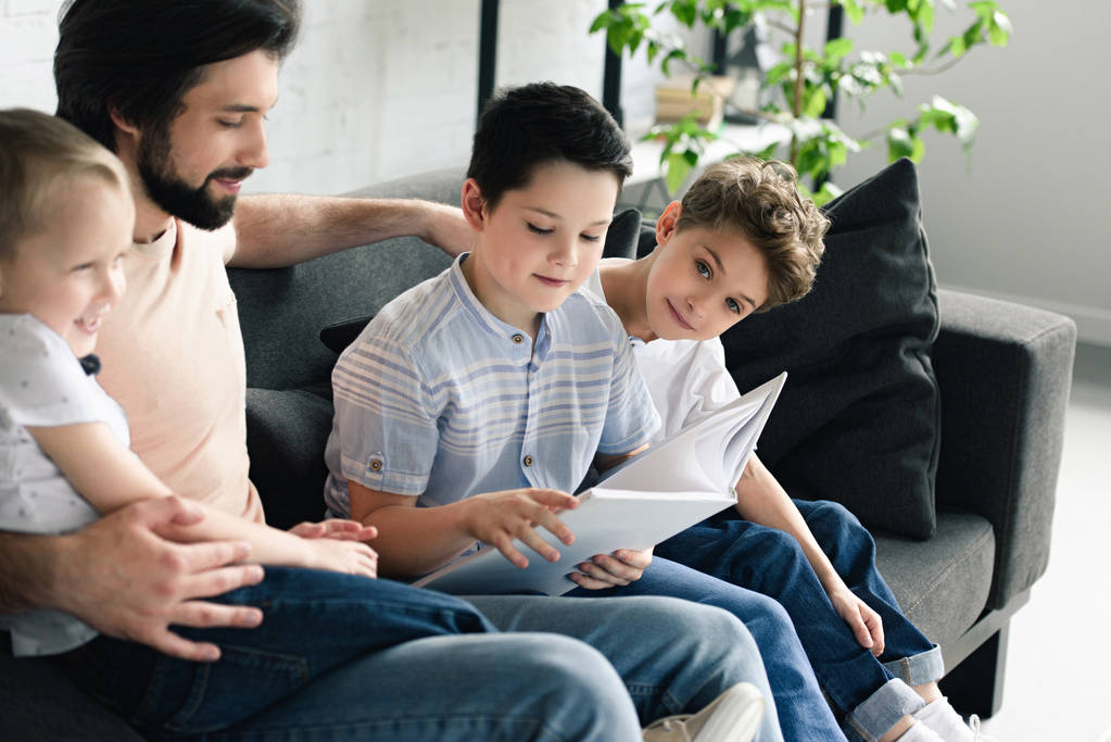 side view of father and sons reading book together at home - Photo, Image