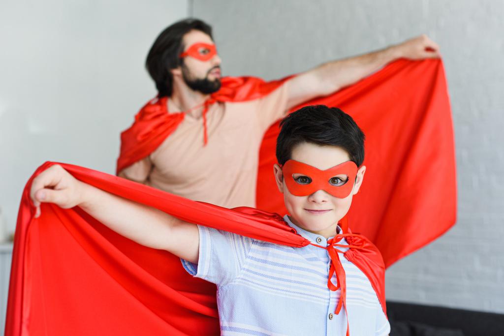 Selektywny fokus małego syna i ojca w czerwony superbohatera kostiumy w domu - Zdjęcie, obraz