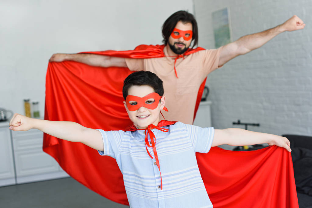 selectieve aandacht van kleine zoon en vader in rode superheld kostuums thuis - Foto, afbeelding