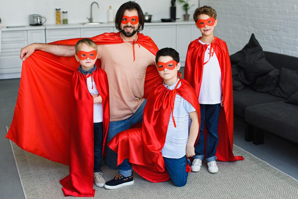 Lächelnder Vater und kleine Söhne in roten Superheldenkostümen zu Hause - Foto, Bild