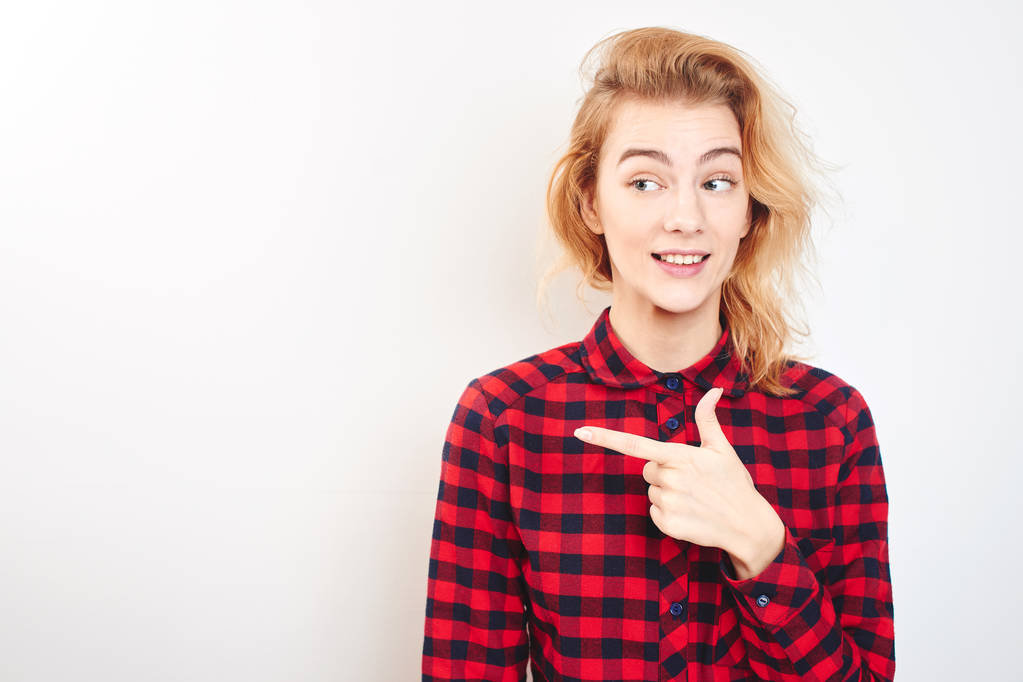 beautiful smiling woman in checkered shirt pointing with finger to left isolated on white background  - Photo, Image