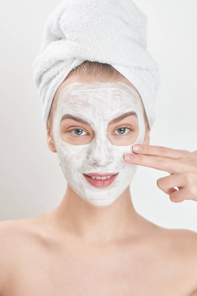 улыбающаяся женщина с полотенцем на голове нанесение маски на лицо, концепция косметических процедур
  - Фото, изображение