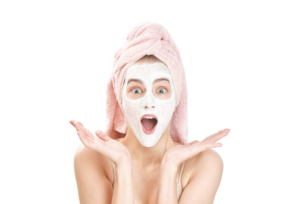 驚いた女性の頭の上のタオルと開いた口、美容治療コンセプトのカメラ目線の顔にマスクを  - 写真・画像