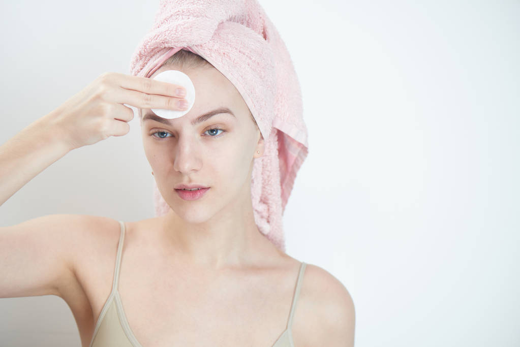 woman with towel on head wiping clean skin with cotton pad on white background - Photo, Image