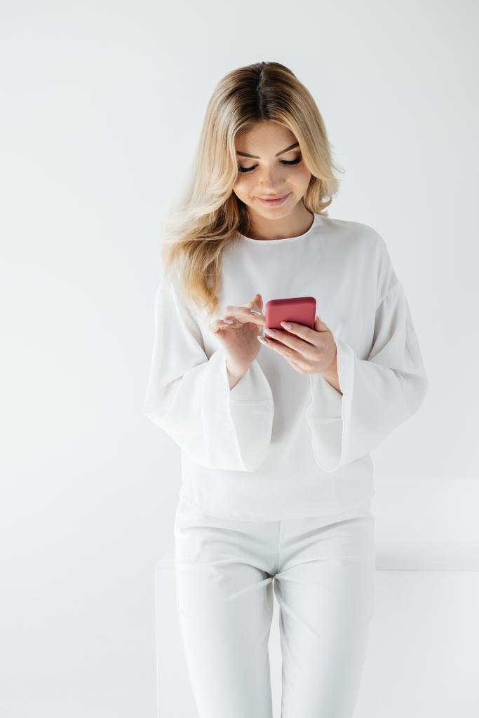 femme blonde souriante en vêtements blancs en utilisant un smartphone isolé sur gris
 - Photo, image