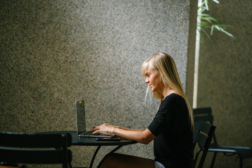 Portret kobiety młody i atrakcyjny biznes blond pracy na jej laptop notebook w kawiarni w ciągu dnia. Siedzi w dół i uśmiechnięty jak ona koncentruje się na swojej pracy. - Zdjęcie, obraz