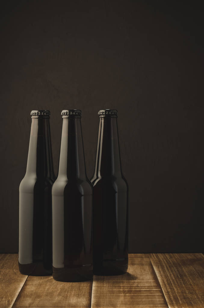 Três garrafas de cerveja de uma prateleira de madeira / Três garrafas de cerveja em um fundo escuro de uma prateleira de madeira
 - Foto, Imagem