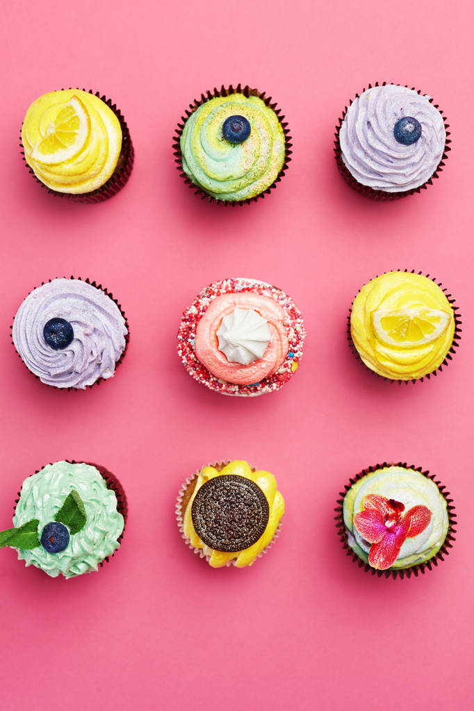 Kleurrijke Cupcakes op roze achtergrond. De Desserts van de cake met slagroom en verschillende Toppings. Hoge resolutie - Foto, afbeelding