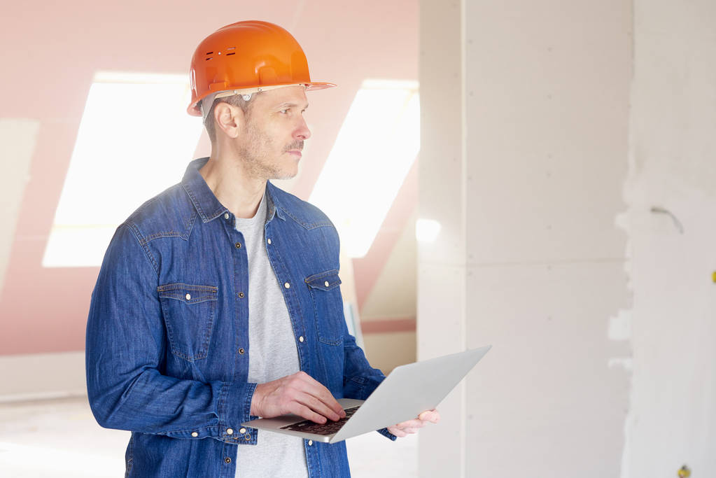 Midden leeftijd bouwvakker laptop houdt in zijn hand terwijl terwijl staande op constraction site en werken. - Foto, afbeelding