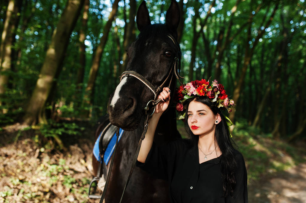 Містична дівчина у вінку одягнена в чорне з конем у дереві
. - Фото, зображення