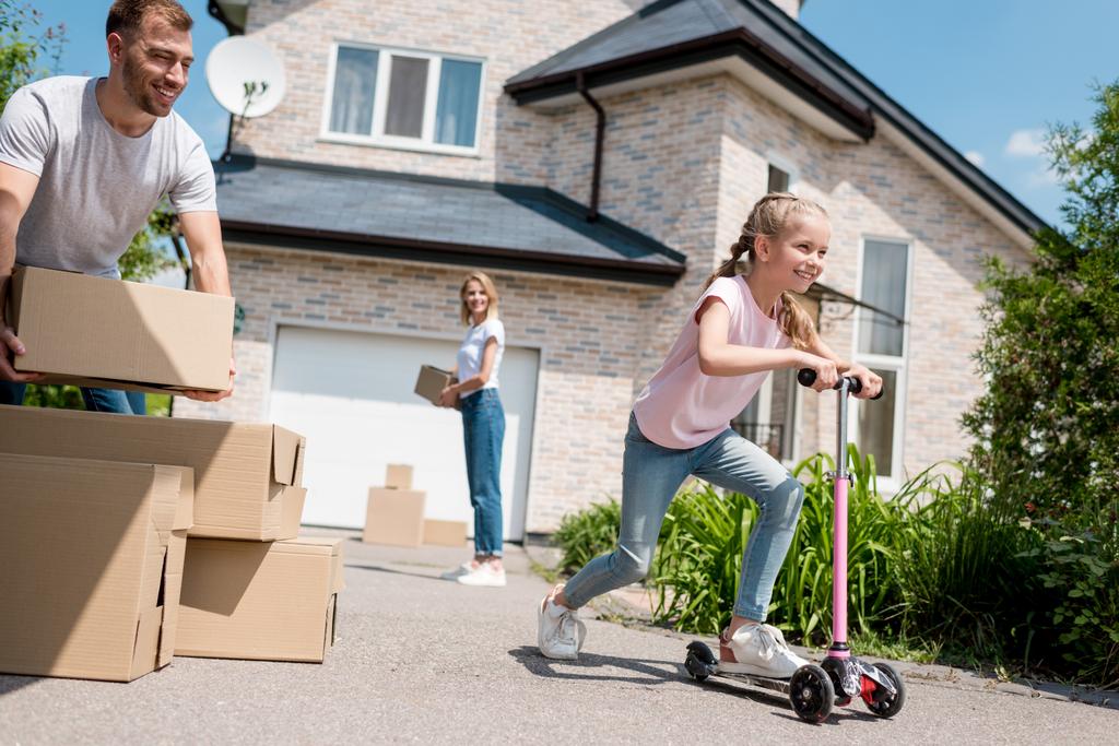 bambino cavalcando su scooter calcio ei suoi genitori disimballaggio scatole di cartone per il trasferimento in una nuova casa
  - Foto, immagini