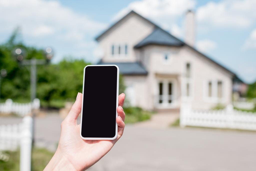 skadrowana młoda kobieta trzymając smartfon z pustego ekranu przed domem  - Zdjęcie, obraz