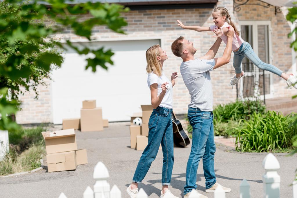 padre crescere figlia mentre la madre in piedi vicino di fronte alla loro nuova casa
  - Foto, immagini