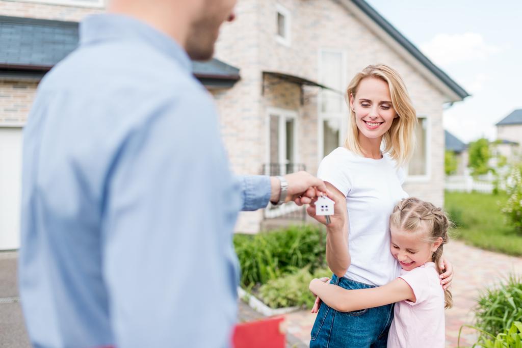 visão parcial do agente imobiliário dando a chave para a jovem com a filha na frente da nova casa
 - Foto, Imagem