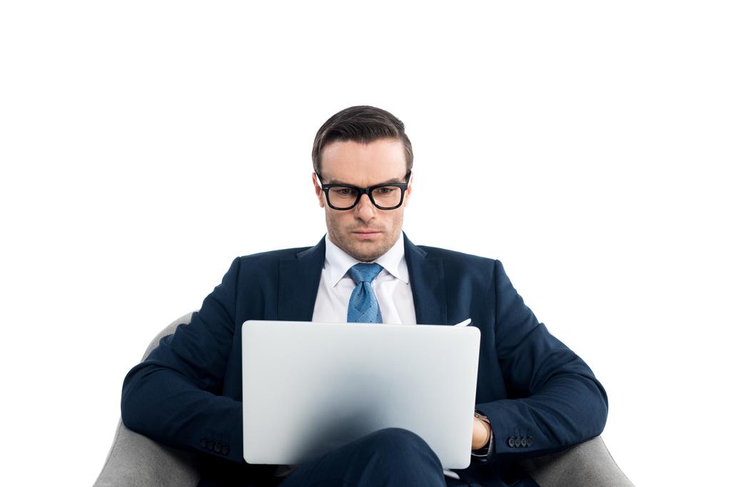 handsome businessman in eyeglasses sitting in armchair and using laptop isolated on white - Photo, Image