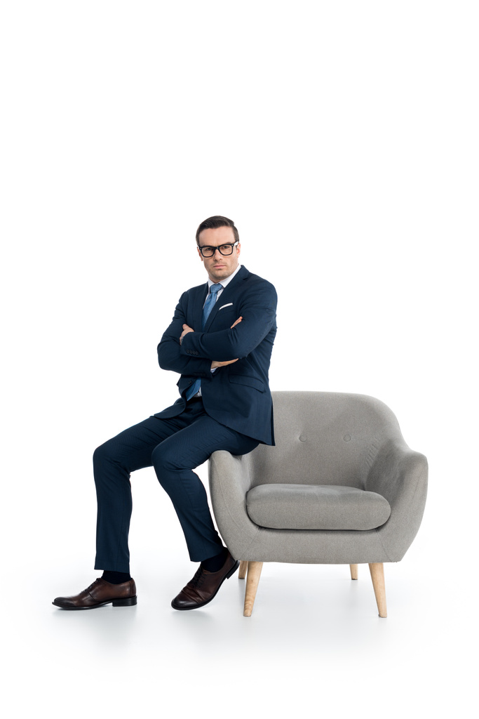 visão de comprimento total de empresário confiante em óculos sentados com braços cruzados e olhando para a câmera no branco
 - Foto, Imagem