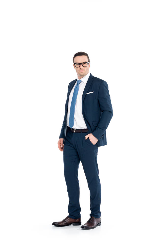 vista completa de hombre de negocios confiado en gafas y traje de pie con la mano en el bolsillo y mirando a la cámara aislada en blanco
 - Foto, imagen