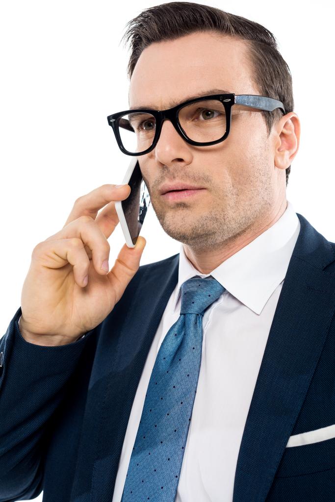 knappe zakenman in brillen praten door smartphone en op zoek weg geïsoleerd op wit  - Foto, afbeelding