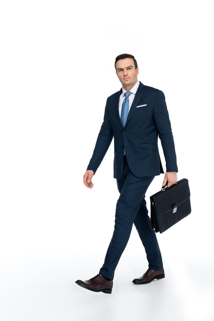 full length view of businessman with briefcase walking and looking at camera on white - Photo, Image