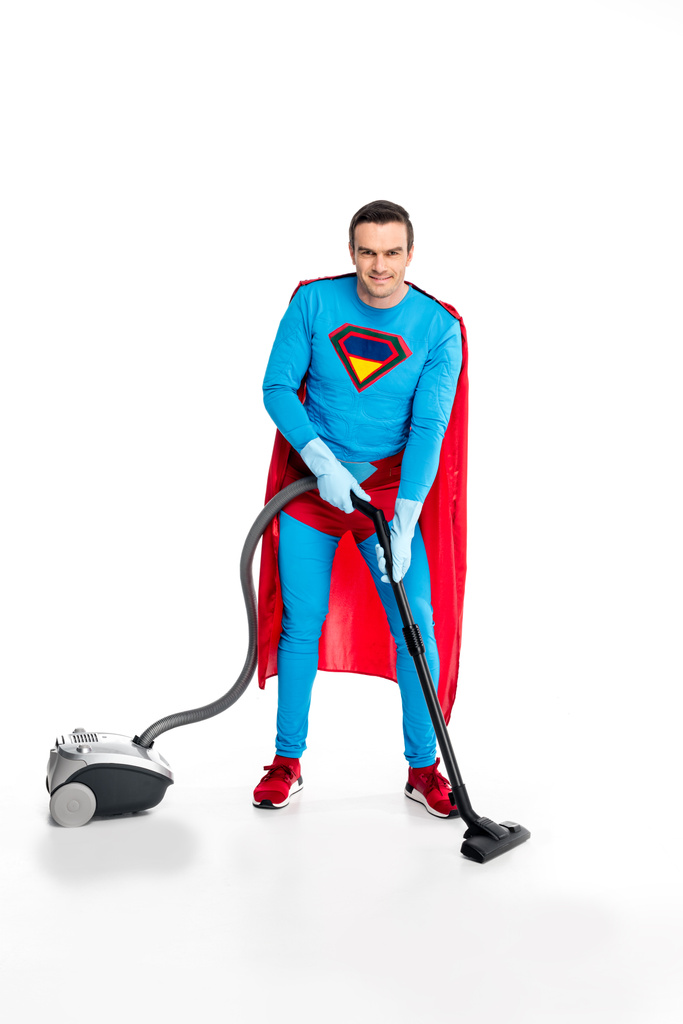 Süpermen elektrikli süpürge kullanarak ve beyaz kameraya gülümseyen lastik eldiven - Fotoğraf, Görsel