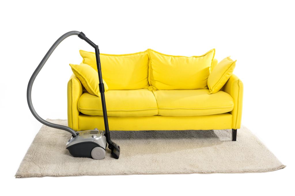 helles gelbes Sofa und Staubsauger auf Teppich isoliert auf weiß - Foto, Bild