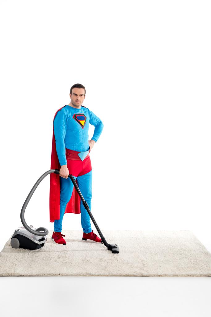 confiado superman limpieza de alfombras con aspiradora y mirando a la cámara aislada en blanco
 - Foto, imagen