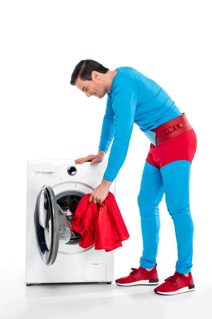 smiling superman washing clothes in washing machine on white - Photo, Image