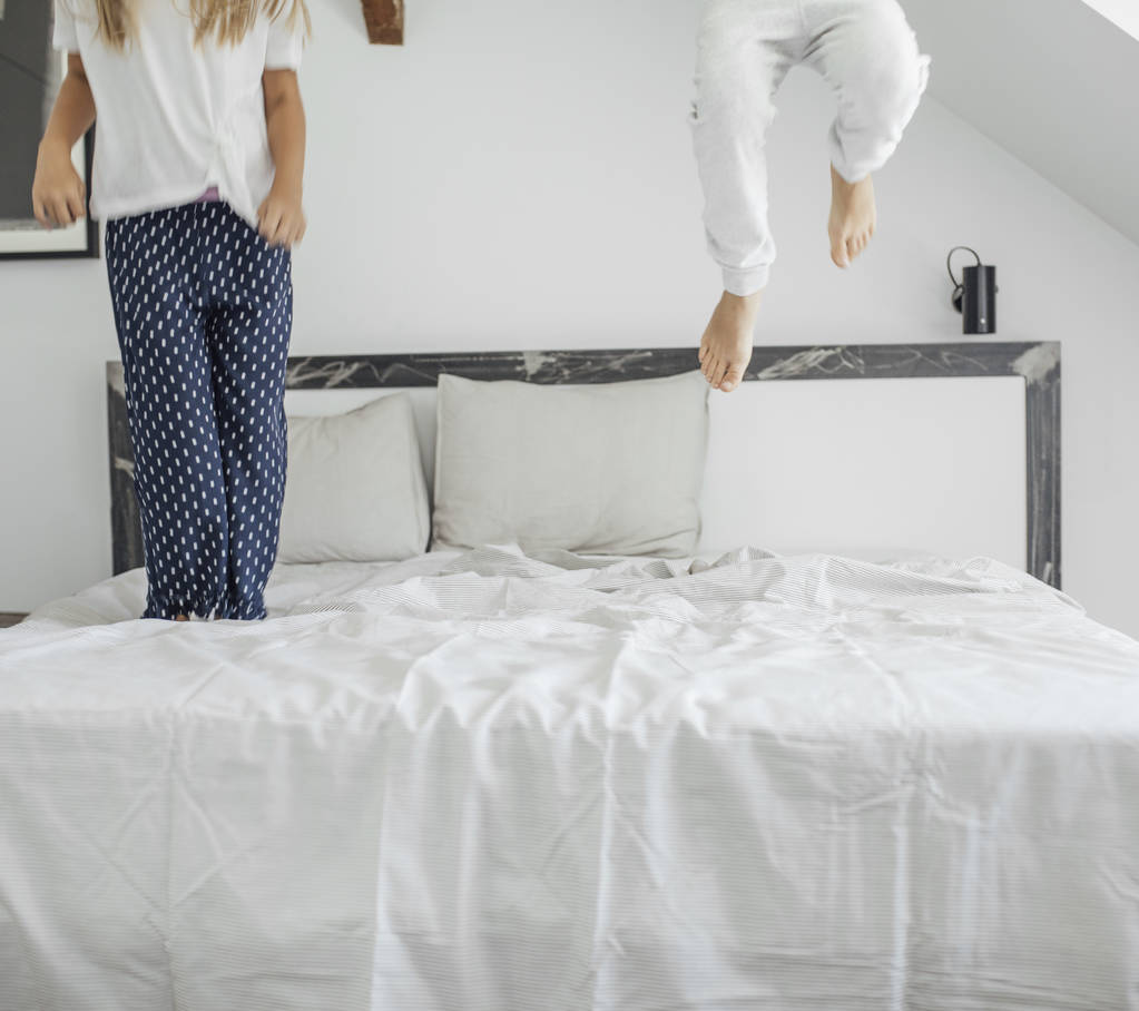 Jambes de deux filles méconnaissables sautant sur le lit en pyjama
. - Photo, image