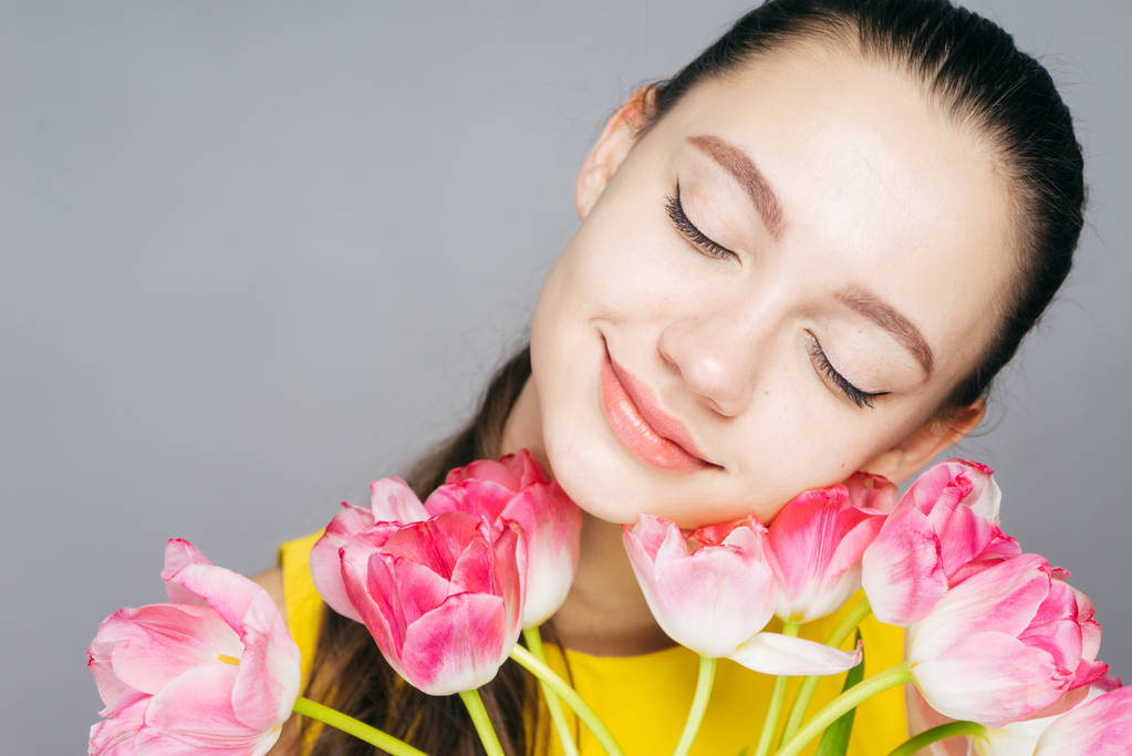 houkutteleva nuori tyttö tilalla kimppu tuoksuva vaaleanpunaisia kukkia, sulki silmänsä, hymyillen
 - Valokuva, kuva