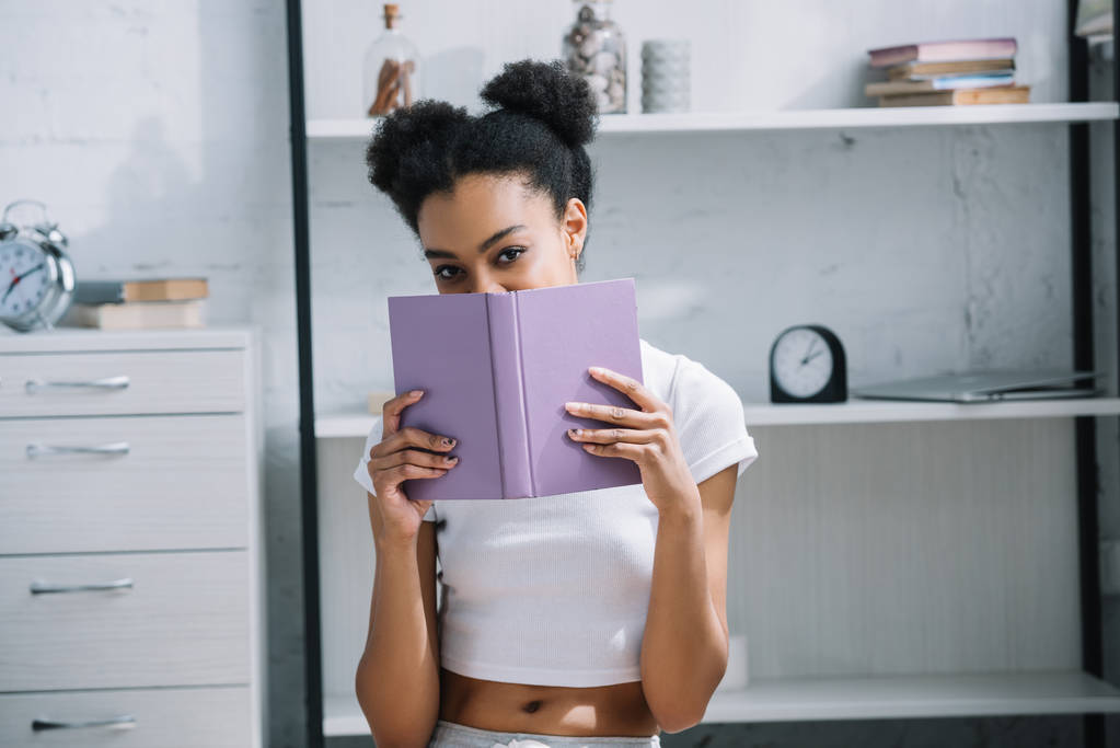 atractivo africano americano mujer estudiante con libro mirando cámara
 - Foto, imagen