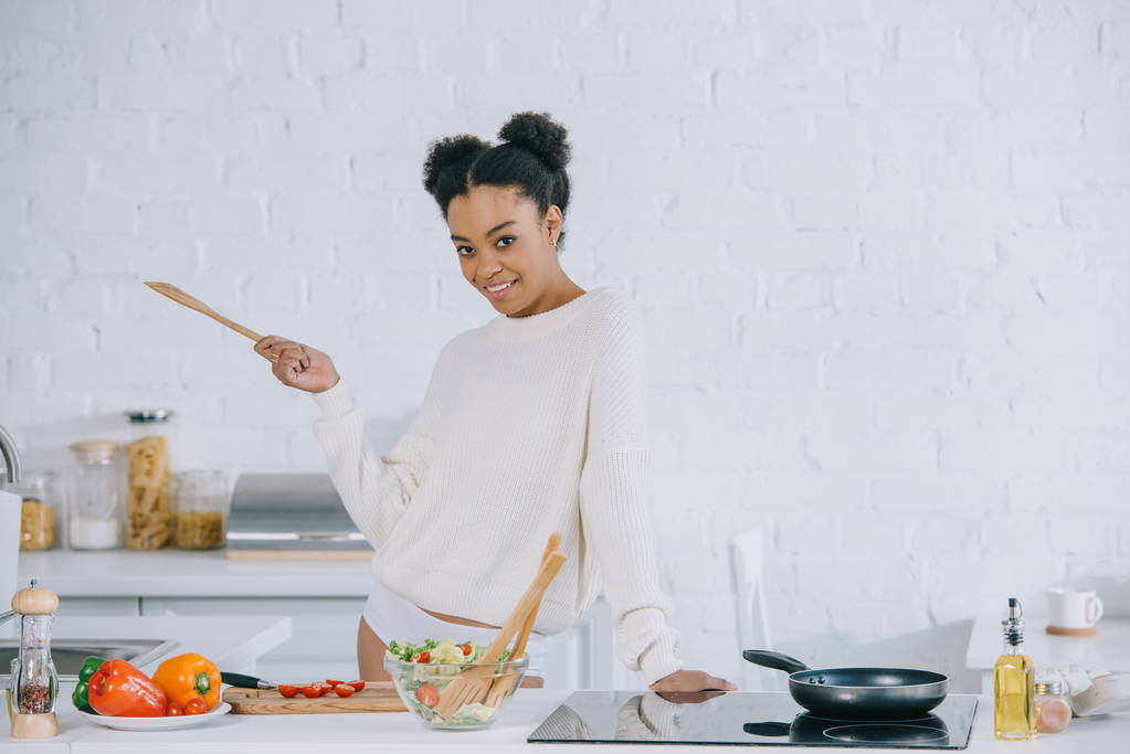 glückliche junge Frau bereitet Frühstück in der Küche zu und blickt in die Kamera - Foto, Bild