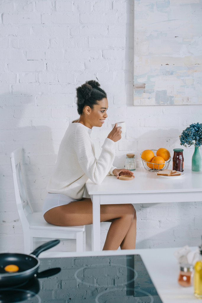 vista laterale di giovane donna sorridente con tazza di caffè del mattino a casa
 - Foto, immagini